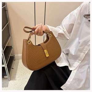 Détail d'un sac selle marron à motif crocodile avec une boucle dorée métallique