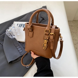 Détail du sac seau en cuir marron avec pendentif ours doré et logo gaufré