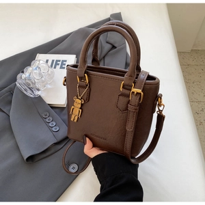 Détail d'un sac cabas en similicuir marron foncé avec un charm d'ours doré et une bandoulière