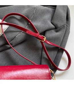 Detail of red wax leather shoulder strap with adjustable gold buckle on fabric