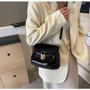 Detail of a black patent leather shoulder bag with a gold triangle mechanical lock