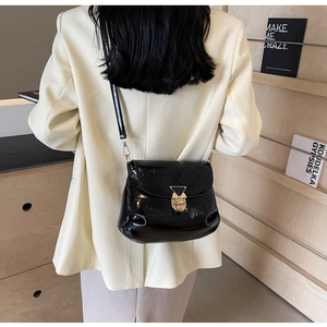 Detail of glossy black patent leather shoulder bag with gold triangle metal buckle