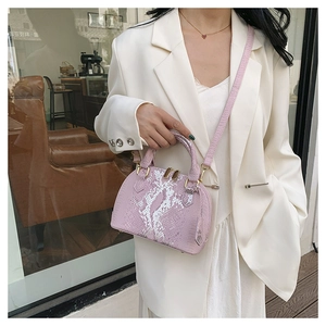 Sac à main rose à motif serpent avec détails dorés porté sur un tailleur blanc