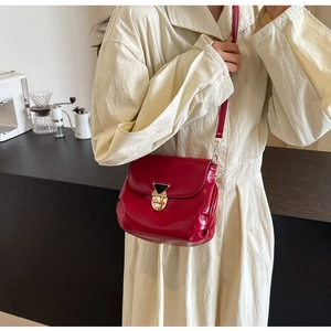 Detail of red patent leather crossbody bag with elegant gold hardware lock and black triangle