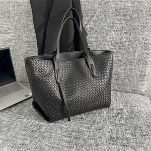 Large black woven tote bag with Intrecciato pattern and dual handles shown on a sofa