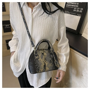 Détail d'un sac coquillage à motif serpent porté en bandoulière avec une chemise blanche