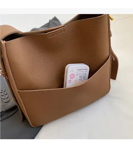 Detail einer braunen Beuteltasche aus Leder mit Narbenstruktur, Seitentasche und Goldschnalle