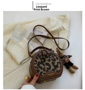 Close-up of a leopard print round crossbody bag with brown leather and gold rivets