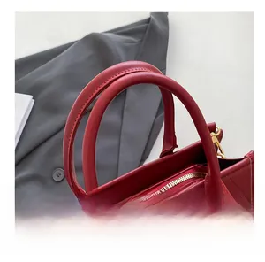 Gros plan détaillé des coutures et ferrures dorées sur un sac cabas rouge texturé
