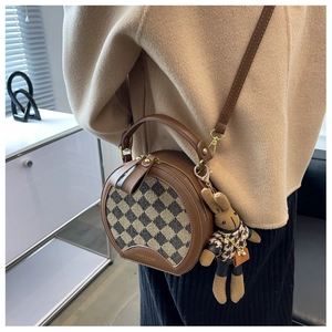 Detail of round crossbody bag featuring checkered fabric and cute rabbit charm accessory