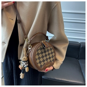 Detail of a brown checkered round handbag with leather trim and woven rabbit pendant