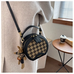 Detail shot of a round crossbody bag with brown checkerboard pattern and bunny charm