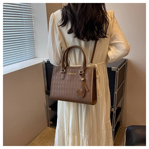 Detail of brown quilted tote bag with gold logo and heart charm on a white dress