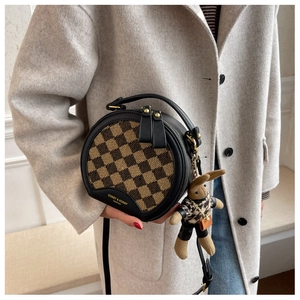 Detail view of round crossbody bag with brown checkerboard pattern and rabbit pendant