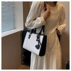 Detail of a black and white quilted tote bag with a heart pendant and golden hardware
