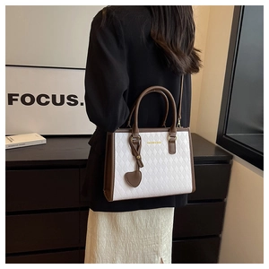 Detail showing the white quilted pattern and heart charm on a brown leather tote bag