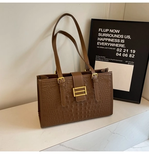 Detail of a brown crocodile pattern tote bag with gold decorative buckle and twin straps