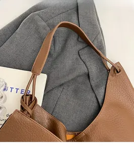 Détail d'un sac cabas en cuir marron montrant une bandoulière large et un nœud décoratif