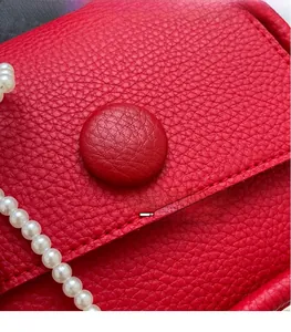 Detail of red lychee textured leather saddle bag with white pearl chain strap