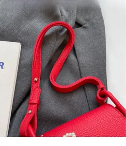 Detail of red lychee grain leather strap with white pearl accents and silver rivets
