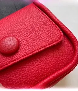 Detail of red lychee textured leather saddle bag with stitching and circular buckle