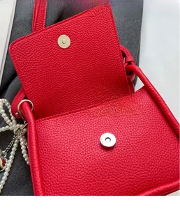 Detail of red lychee grain leather saddle bag featuring silver magnetic buckle and pearls