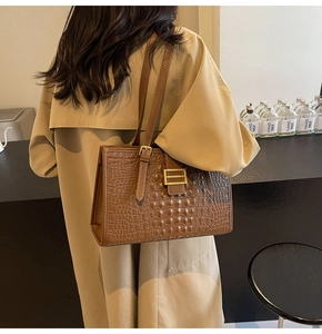 Detail of brown crocodile pattern shoulder bag with a gold buckle on khaki trench coat