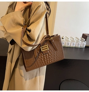 Detail of a brown crocodile pattern tote bag with golden buckle and adjustable straps