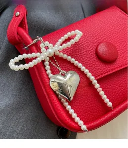 Detail of pearl bow and heart charm pendant on red lychee texture saddle bag