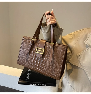 Detailed close-up of brown crocodile texture tote bag with golden metal buckle clasp