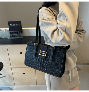Detail of black crocodile embossed leather shoulder bag with gold square metal buckle