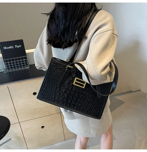 Detail of black crocodile pattern tote bag with gold buckle worn by model in casual style
