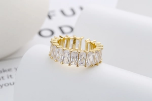Détail d'une bague ouverte dorée sertie de zircons sur papier blanc texturé