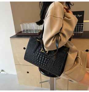 Close-up of black crocodile-embossed leather tote bag with gold buckle detail