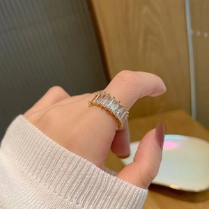 Gros plan d'une bague dorée ornée de cristaux taille baguette, portée à la main sur fond zen