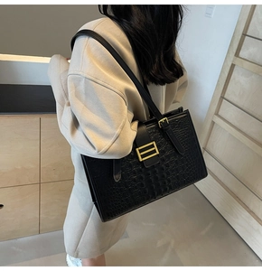 Detail of black faux crocodile leather tote bag with a golden rectangular clasp buckle