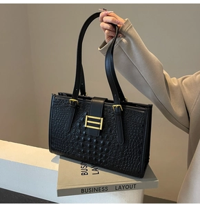 Detail of black crocodile texture handbag with golden buckle and sleek leather handle