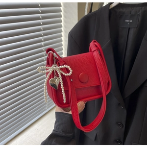 Detail of red lychee textured saddle bag with pearl bow and metal heart charm