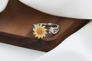 Detailed view of adjustable sunflower ring with orange zircons on a textured wood block