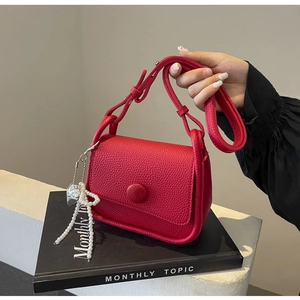 Detail of red lychee textured saddle bag with pearl heart pendant and adjustable strap