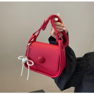 Close-up of red lychee textured saddle bag featuring a pearl and silver heart charm