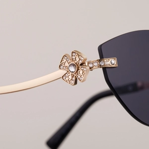 Détail de la charnière trèfle dorée sertie de cristaux sur lunettes de soleil œil-de-chat