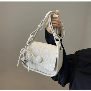 Close-up of white lychee pattern leather saddle bag with pearl bow and silver heart charm