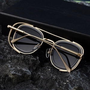 Close-up of golden dual-bridge metal frame sunglasses with black lenses on a rock surface