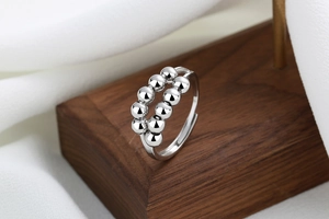 Macro detail of silver rotating double-bead anxiety ring on dark walnut wood stand