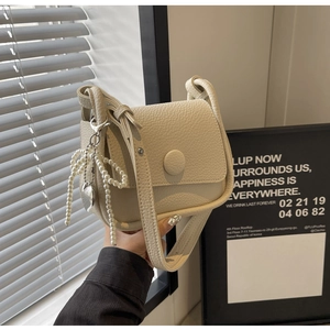 Close-up of creamy white lychee grain leather saddle bag with pearl bow charm and round buckle