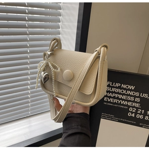 Detail of lychee textured cream crossbody bag with a pearl bow and heart charm