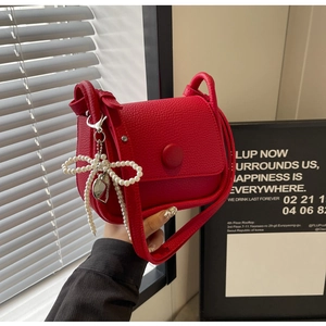 Close-up of red lychee pattern leather saddle bag with pearl bow and heart charm details