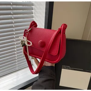 Detail of red lychee grain leather saddle bag featuring pearl heart charm and strap