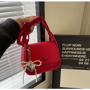 Close-up of red pebble leather saddle bag with pearl bow and heart pendant detail